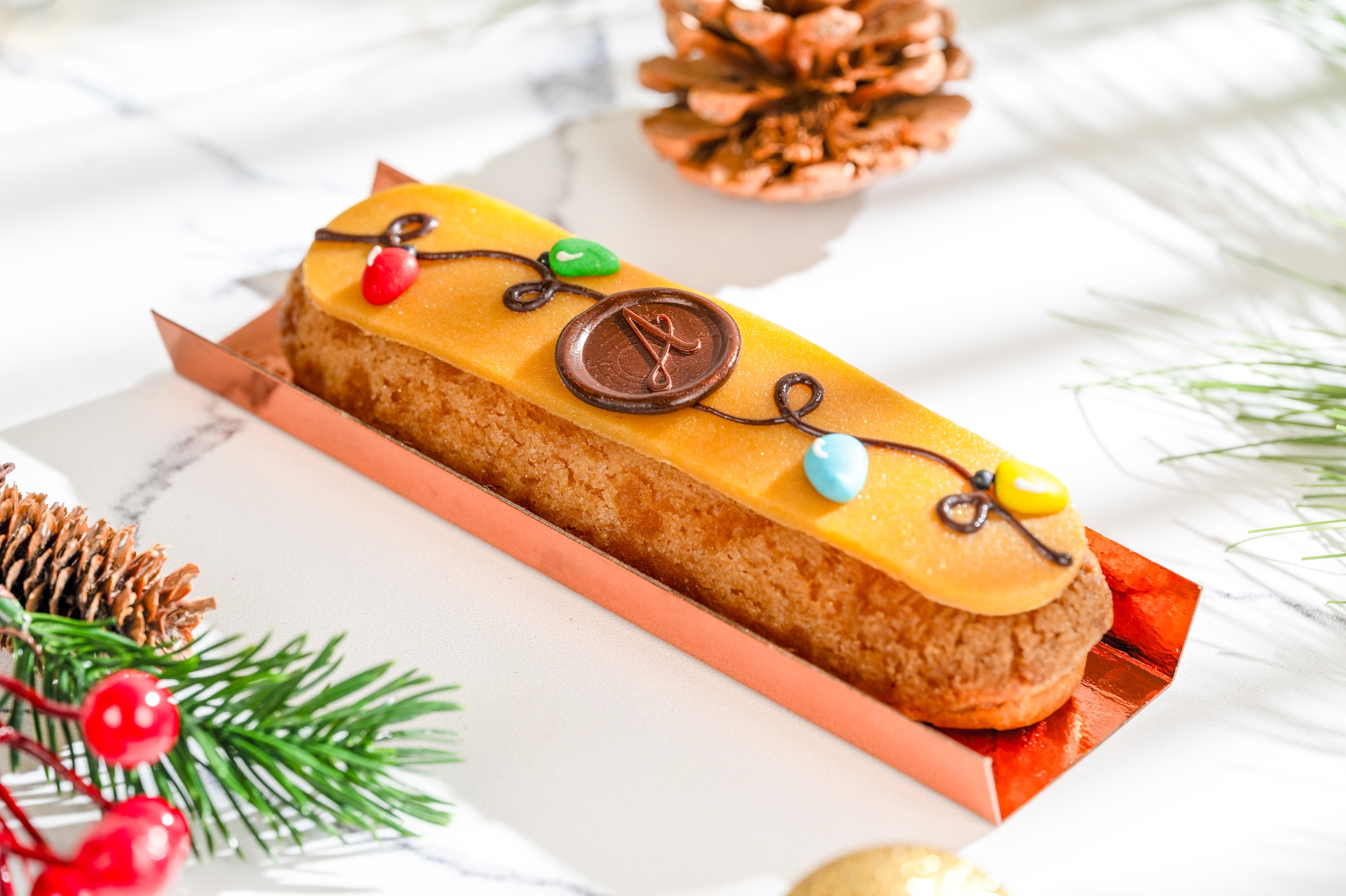 Vanilla Éclair: Pâte à choux filled with vanilla mousse topped with marzipan, sugar Christmas lights, and a chocolate coin (New) 