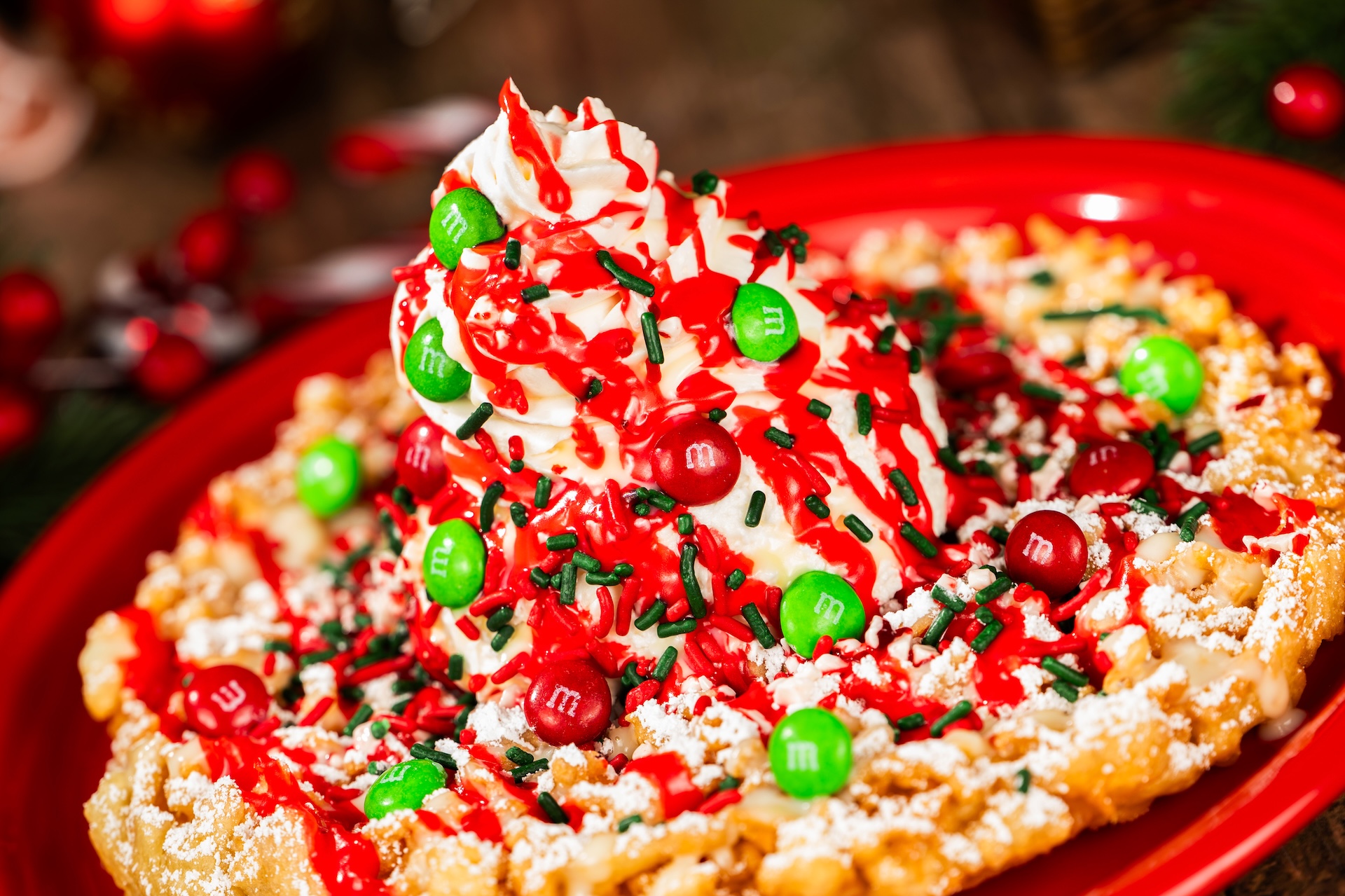 Peppermint Bark Funnel Cake topped with vanilla ice cream, peppermint and white chocolate sauces, M&M'S Milk Chocolate Candies Holiday Blend, whipped cream, crushed peppermint, and festive sprinkles