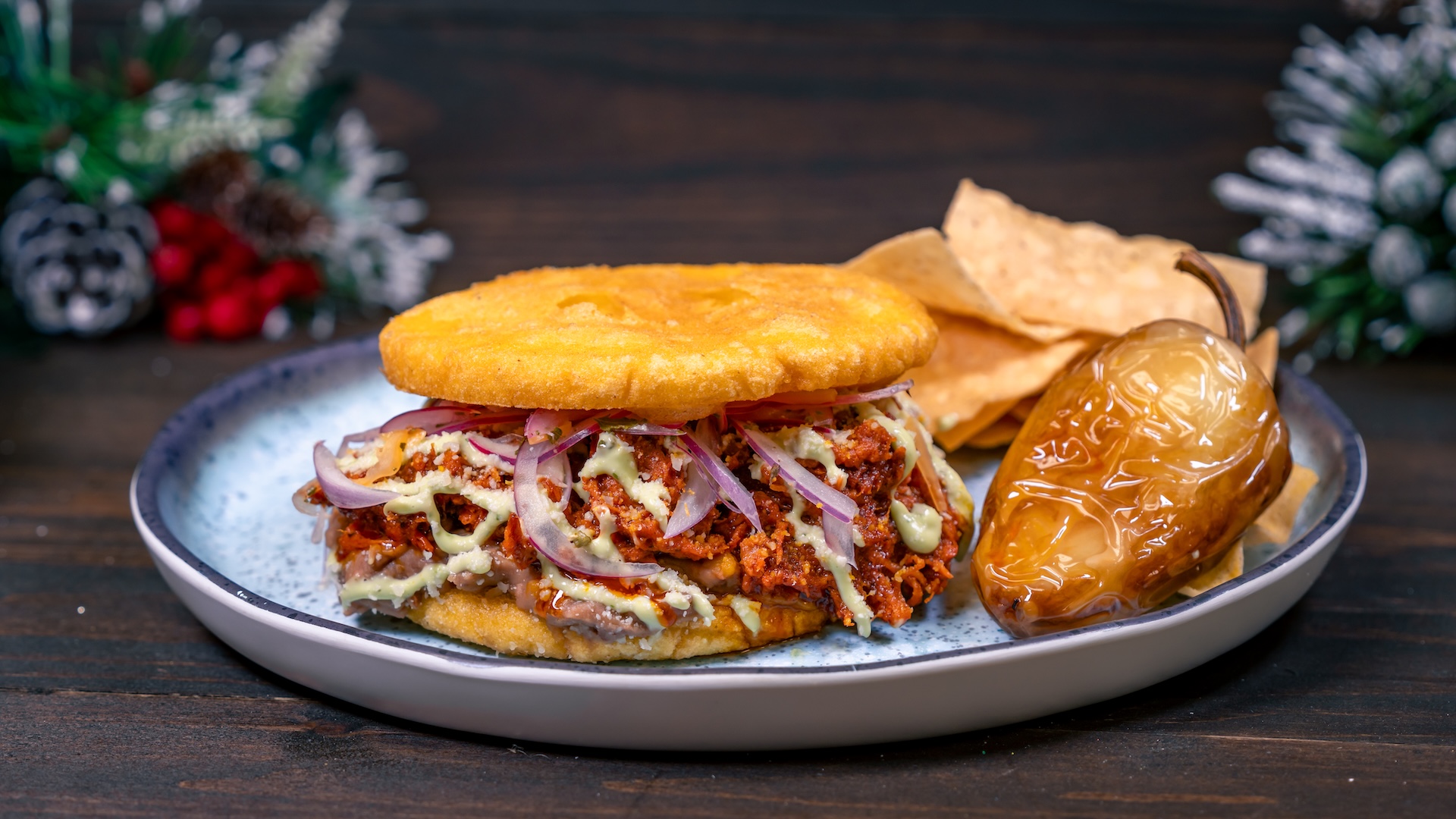 Arepa de Cochinita Pibil: Crispy corn arepa with refried beans, cochinita pibil (Yucatán Peninsula-inspired Pulled Pork), avocado salsa, cotija cheese, and spicy pickled red onions served with tortilla chips (New) 