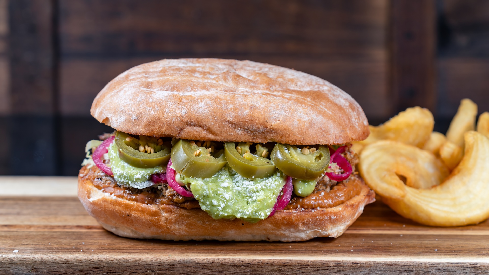 Yuletide Carnitas Torta: Warm telera bread with carnitas, chorizo beans, cotija, lettuce, pickled onions and jalapeños, and guacamole spread served with fries (New)  