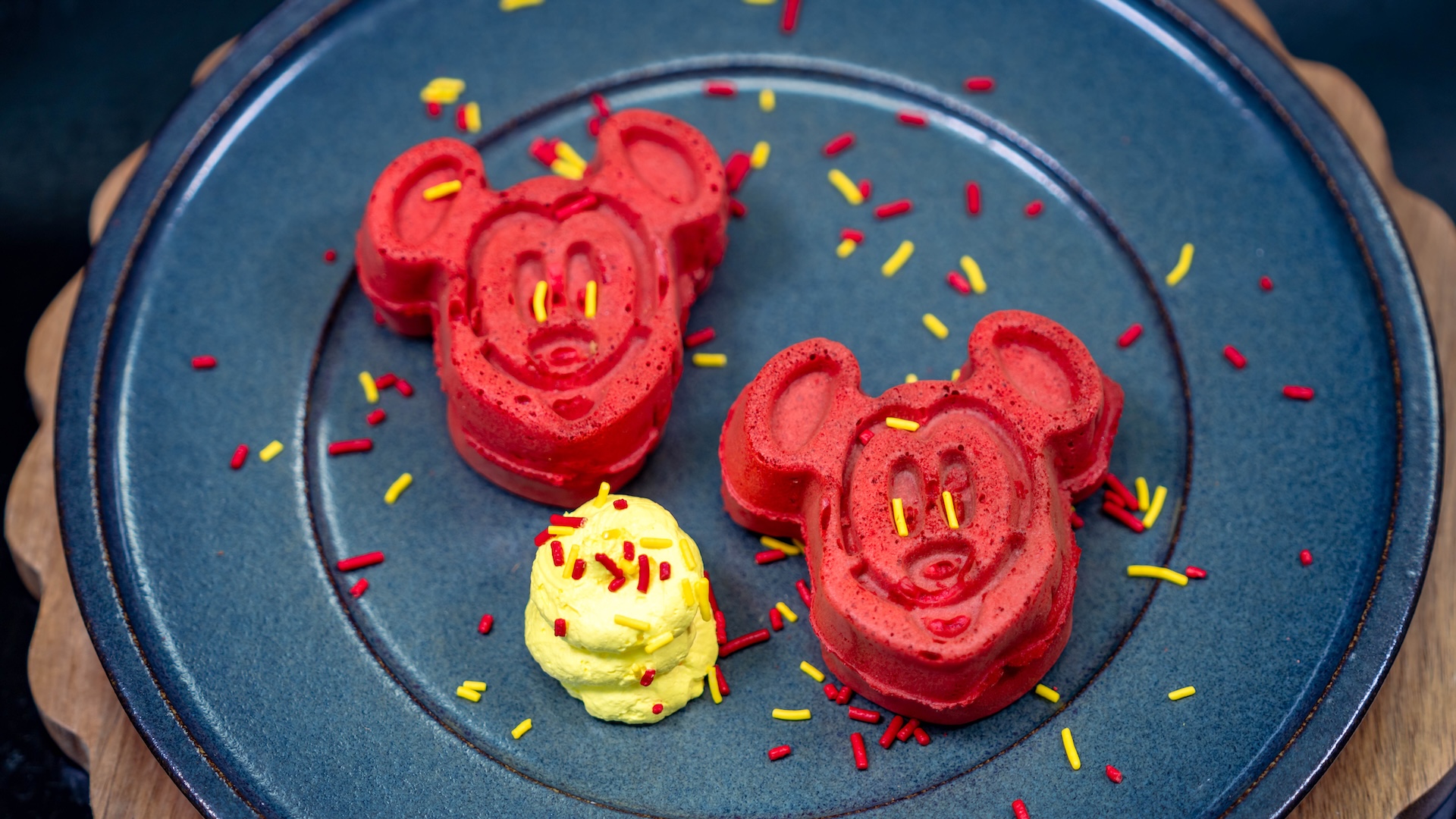 Hotteok-Inspired Mickey-shaped Waffles: Red batter waffles with brown sugar and cinnamon custard, yellow whipped topping, and sprinkles (New)