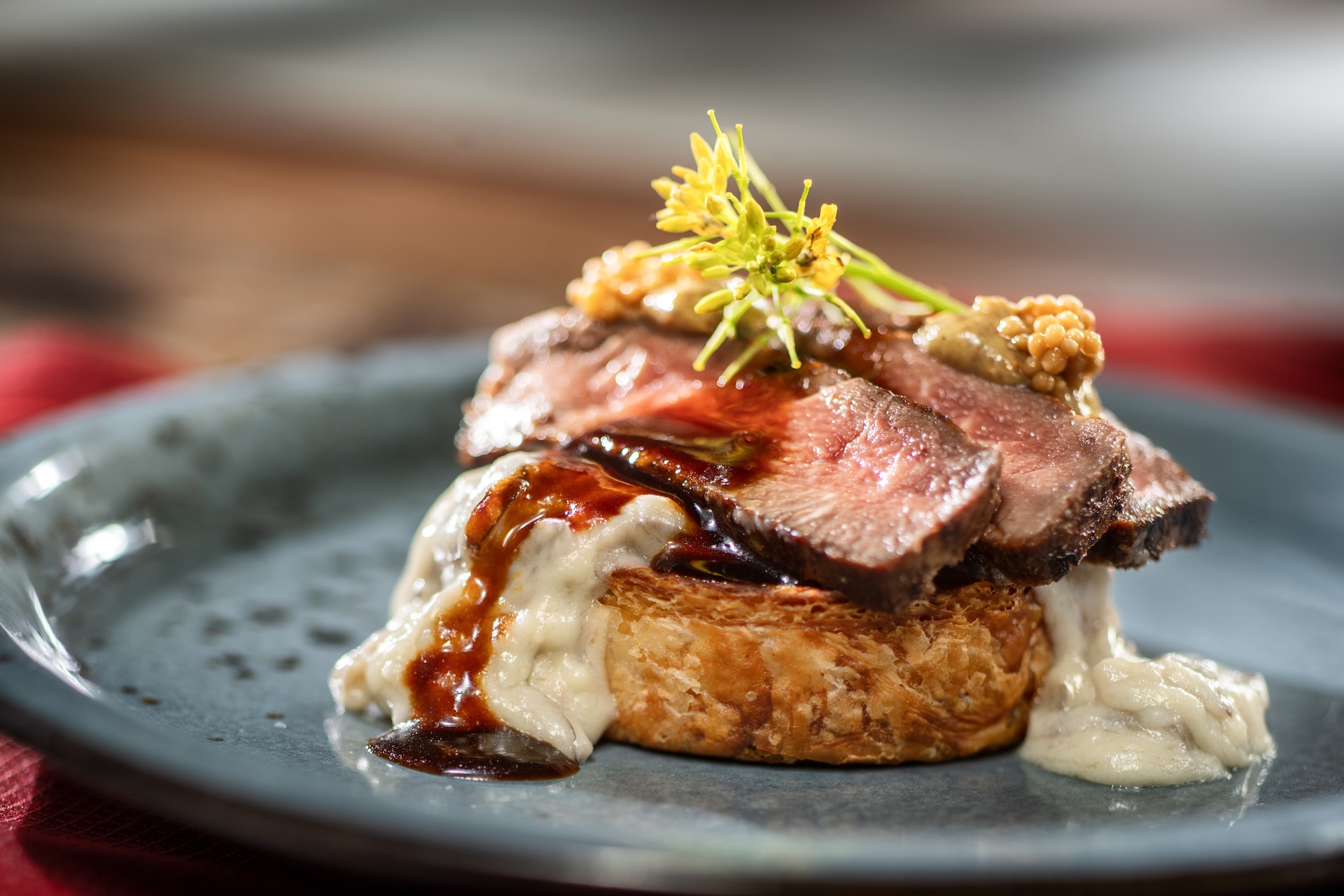 Beef Wellington-inspired Croissant Supreme with creamed spinach croissant pinwheel, mushroom-gorgonzola ragoût, mustard-grilled flank steak, red wine sauce, and pickled mustard seeds